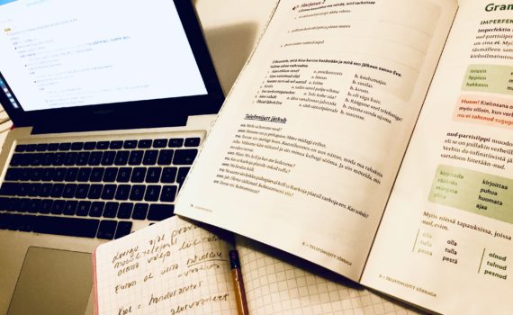 Pöydällä tietokone, vironkielen oppikirja ja vihko, jossa merkintöjä