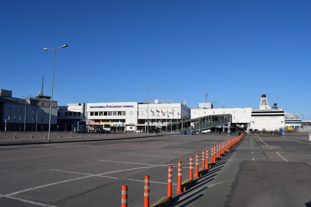 A-Terminal Tallinnassa, keskellä tyhjä parkkipaikka ja horisontissa siintää valkoisia rakennuksia. Keskellä kuvaa punaisia liikennekartioita.