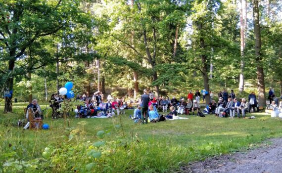 Puistonäkymä, jossa istuu ihmisiä vilteillä, laulamassa yhdessä.